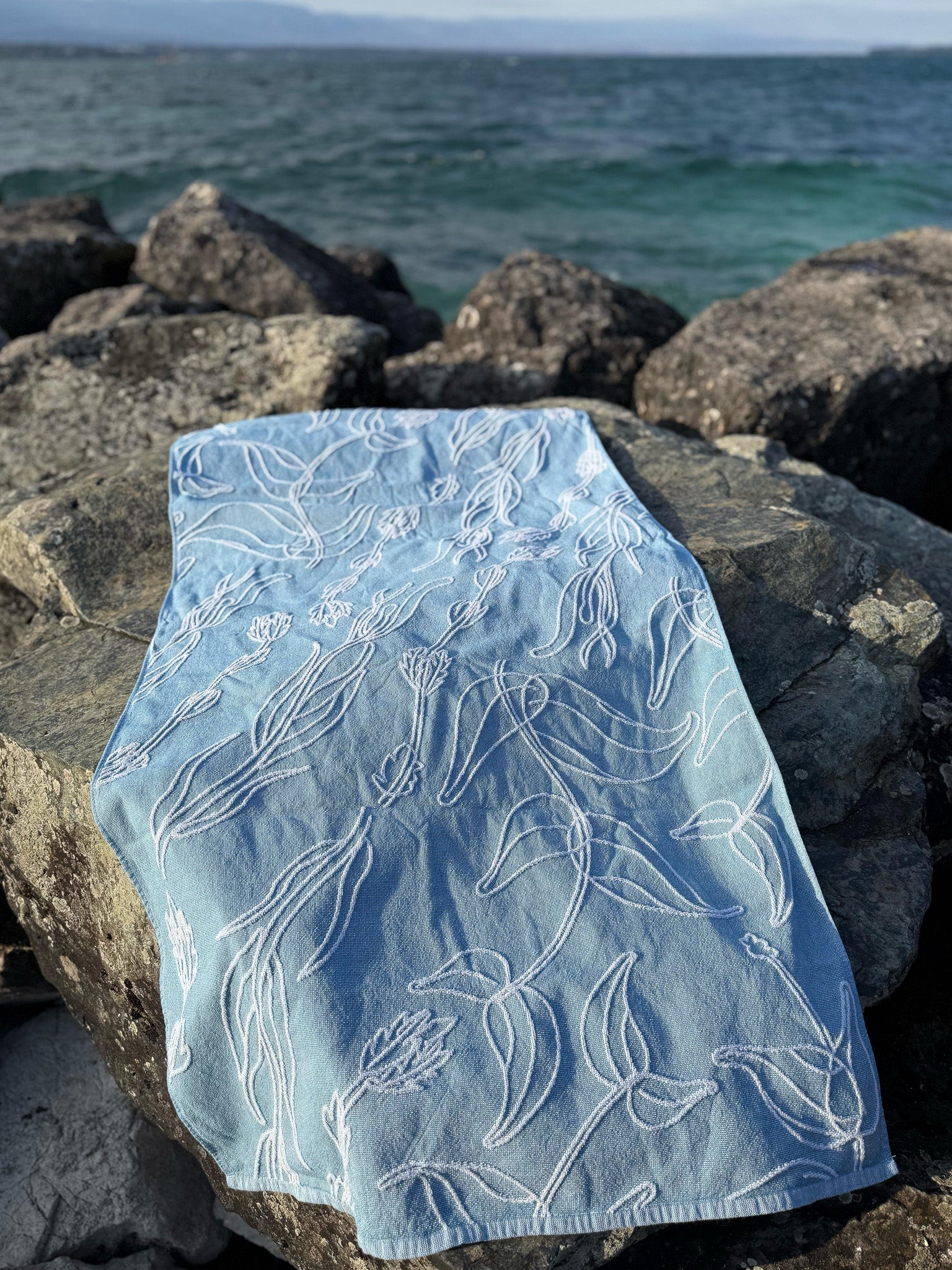 Light blue fabric with aquatic plant patterns on rocks by the water