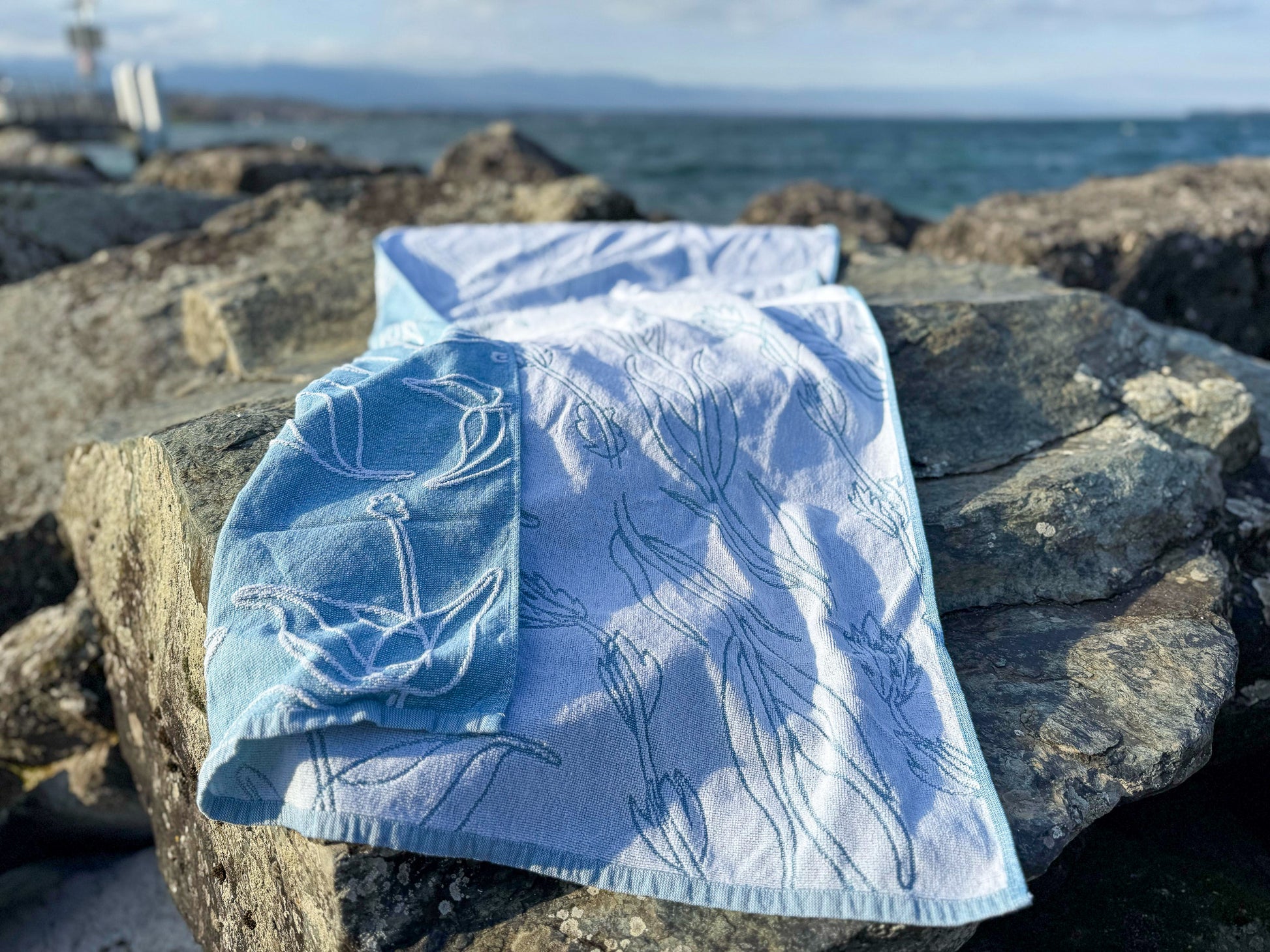 Folded blue and white towel with aquatic plant pattern on a rock by the water