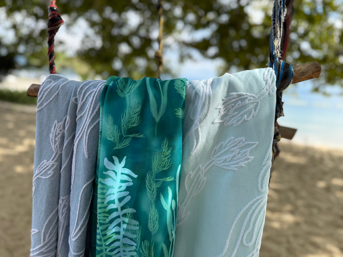 Three beach towels with aquatic plant patterns hanging off a swing