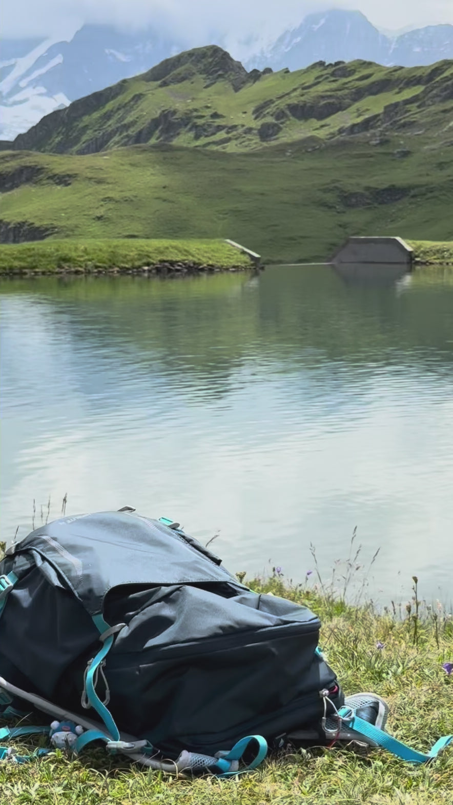 Folded blue-green Traveler beach towel is packed easily into a hiking backpack. Mountain and lake scenic background.